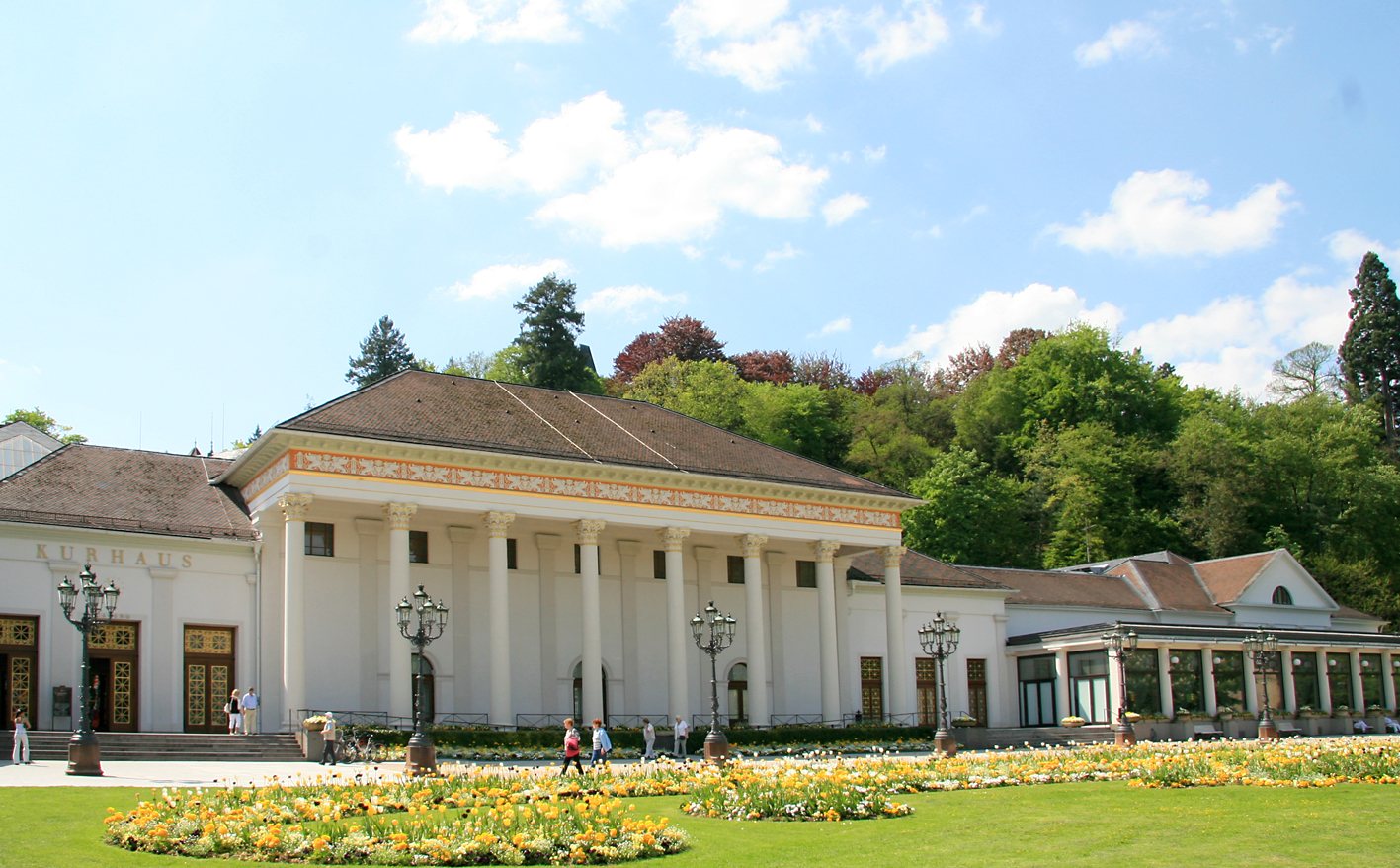 Das Kurhaus in Baden-Baden: ein weißer Bau mit Säulen und vergoldetem Fries, Laternen und Blumenbeete im Kurgarten